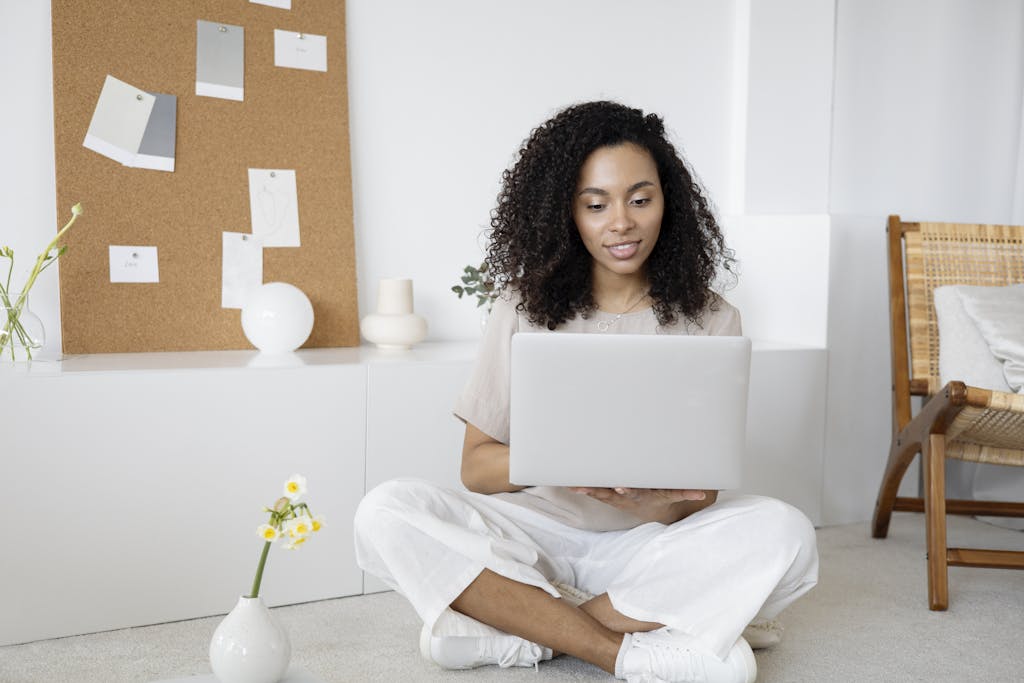 Accueil Young woman with curly hair working on her laptop in a cozy home setting, exuding confidence and focus.